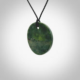 A lovely disc design with cupping on one side and the lightly convex form on the other - a little feature that captures the light and gives the piece a sense of movement and form. Hand made from New Zealand Jade by Ric Moor. Delivered with an adjustable black cord.